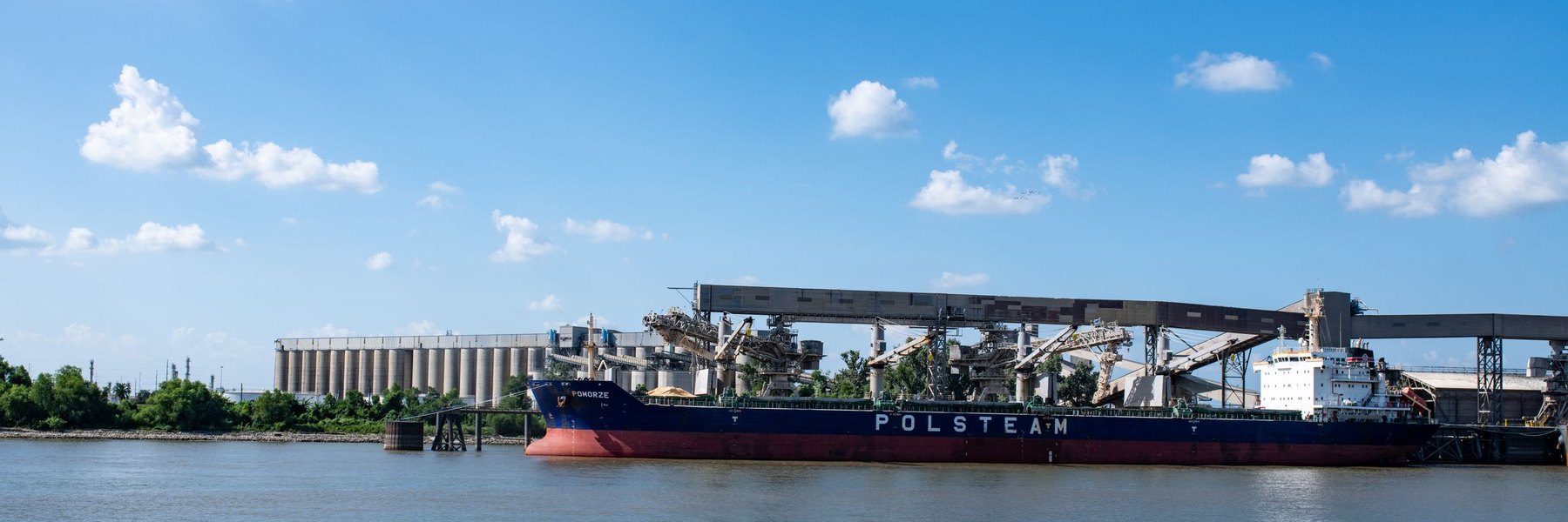 A bulk carrier moored alongside a grain terminal, silos and loading gantries behind it.