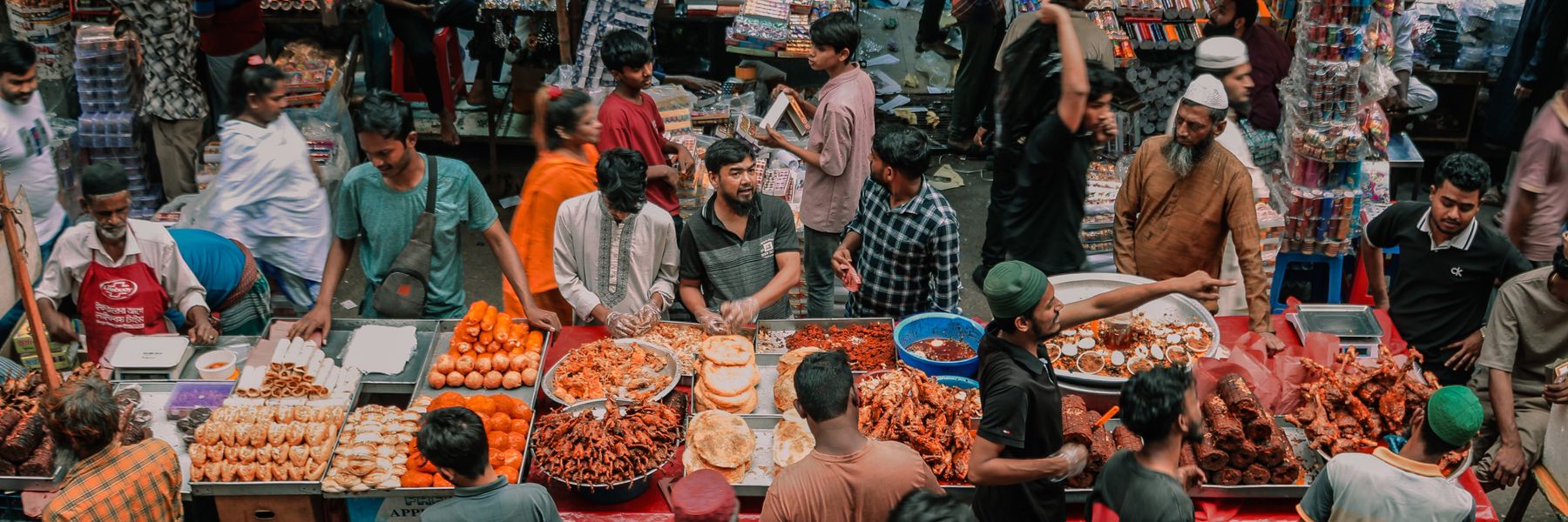 A busy street food market, with shoppers crowded around stalls of fried snacks.