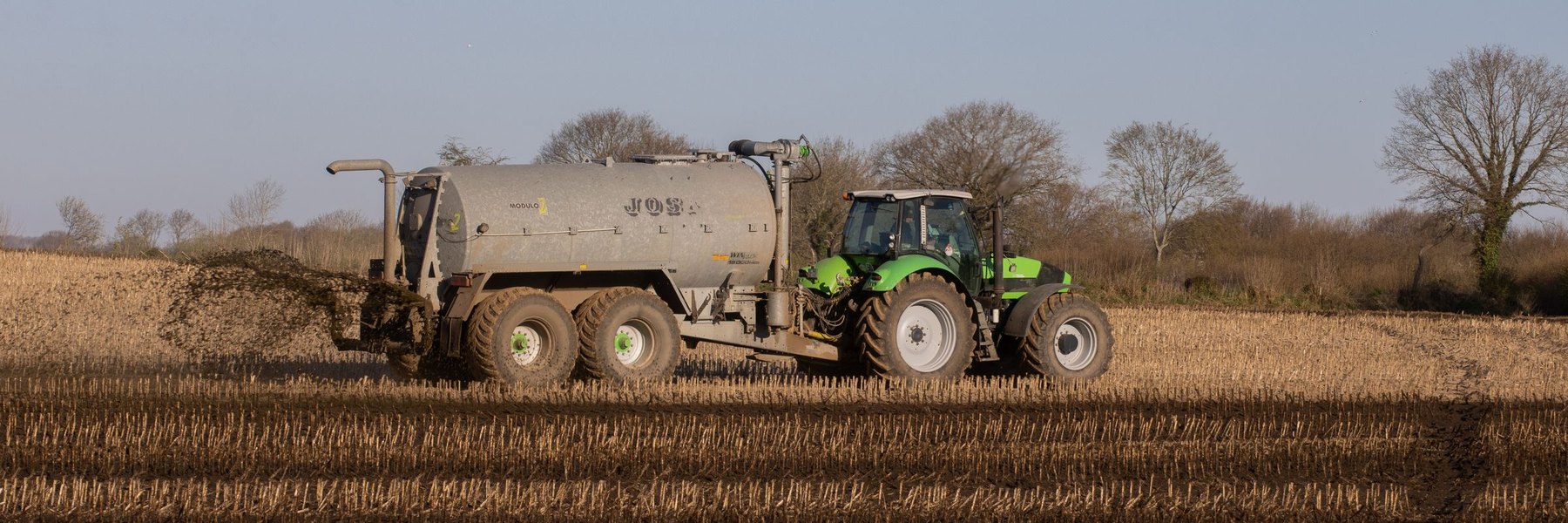 A tractor spreading fertiliser over a freshly ploughed field.