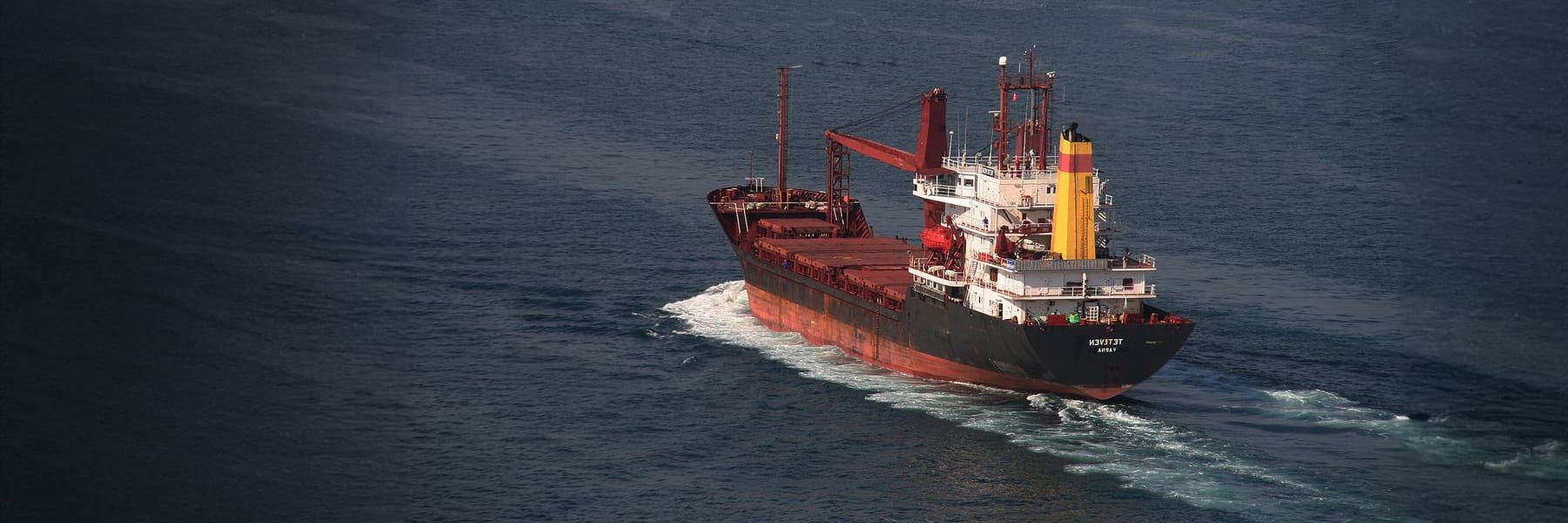 A cargo ship crossing a dark sea, seen from the air.